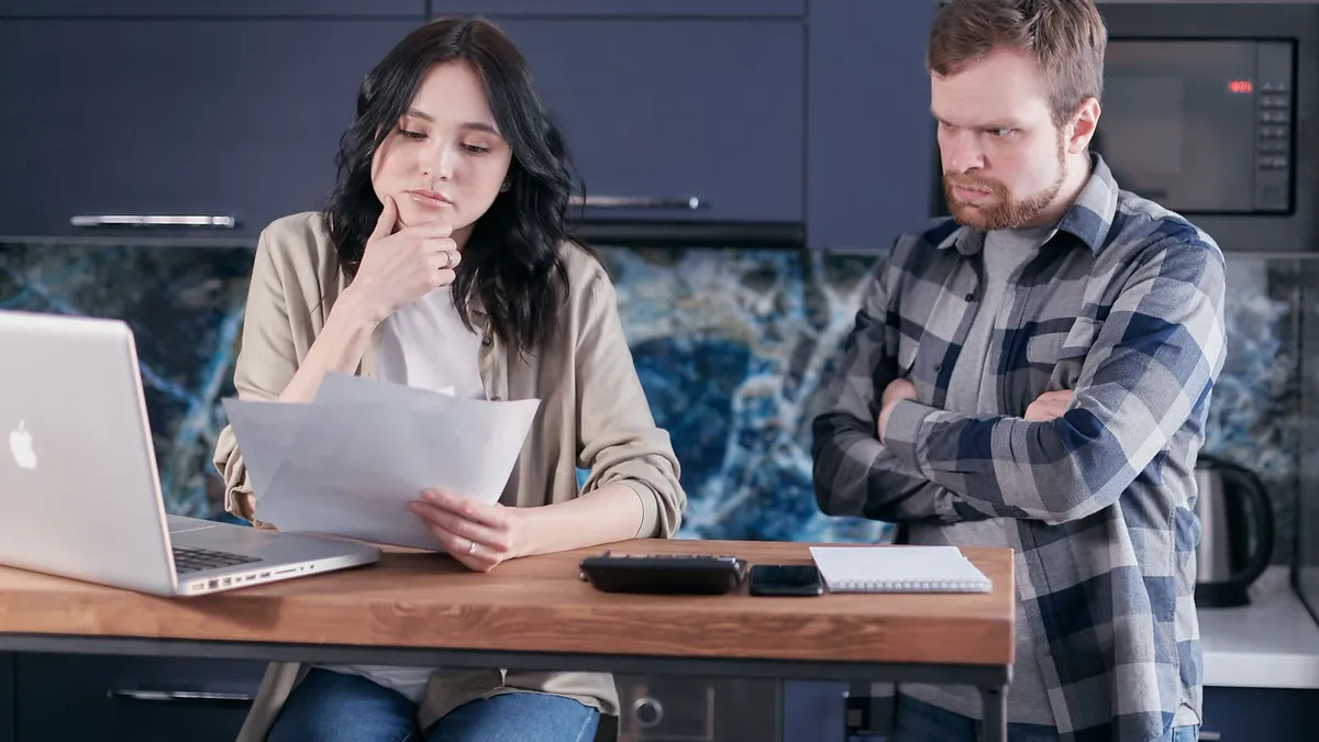 Couple at a kitchen table reviewing a statement with a laptop and calculator to trace a CPC SCP charge