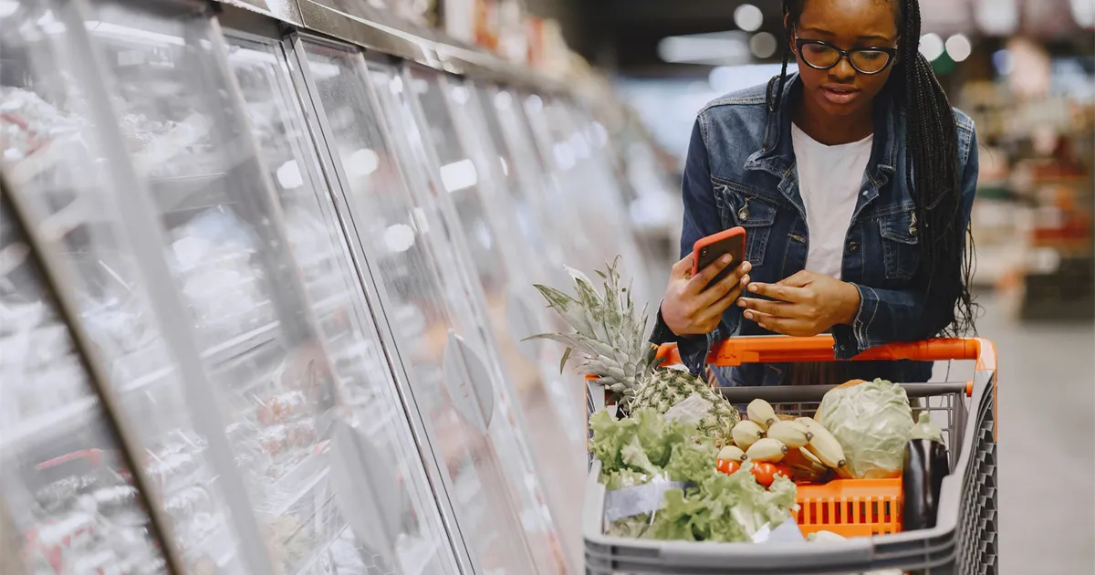 Shopper comparing cashback credit cards on her phone beside a full grocery cart